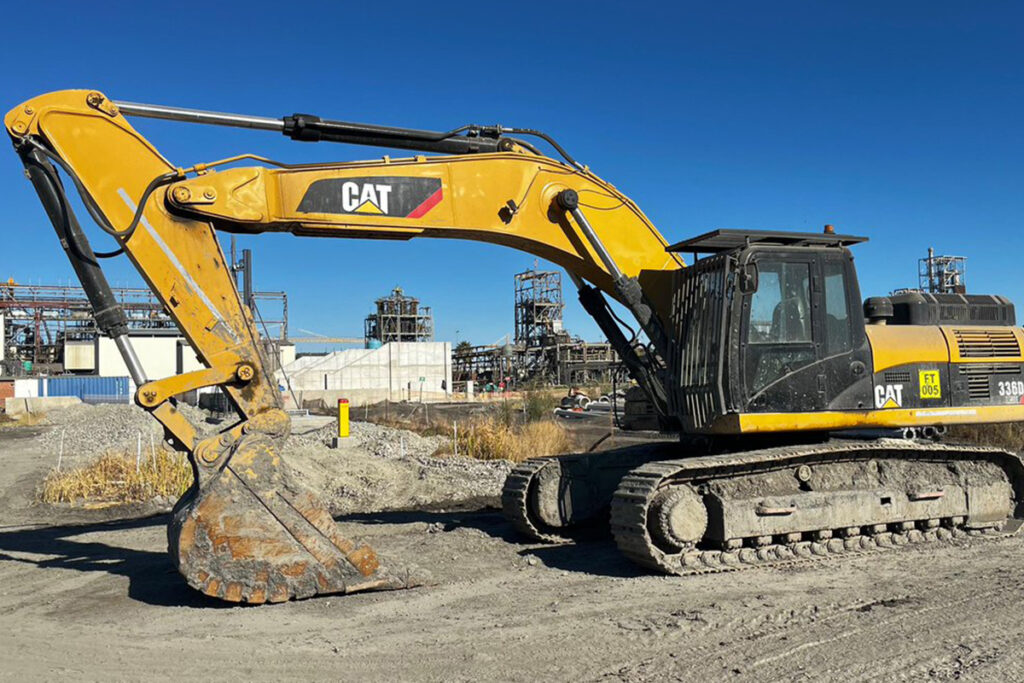Yellow excavator parked in gravel infront of a gate to a site