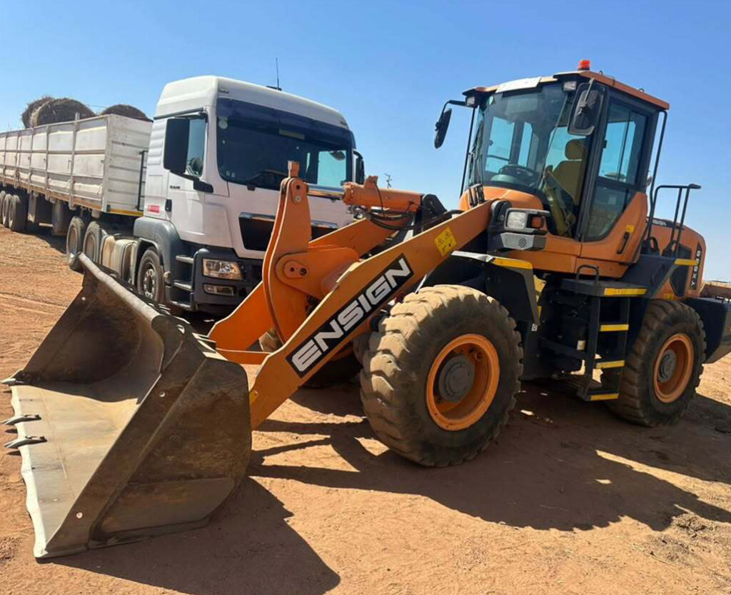 Orange front end loader in front of a white truck