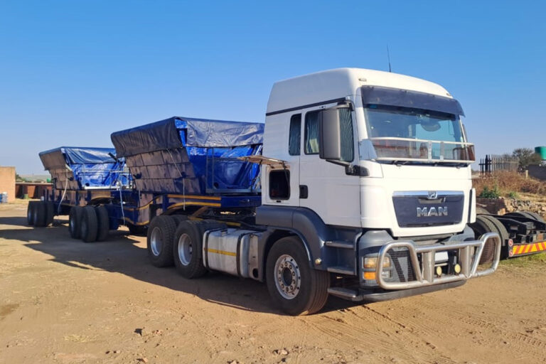 White truck with blue 34ton side tipper trailer parked in a truck yard