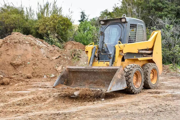Yellow skid steer parked on a patch of gravel