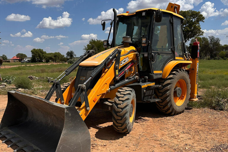Yellow backhoe (tlb) parked on a patch of gravel in a field