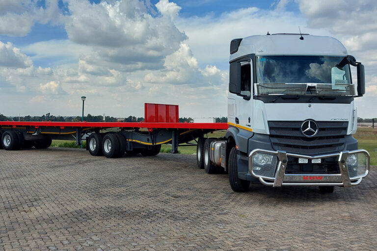 White trck with a red flatdeck trailer parked in a truck yard