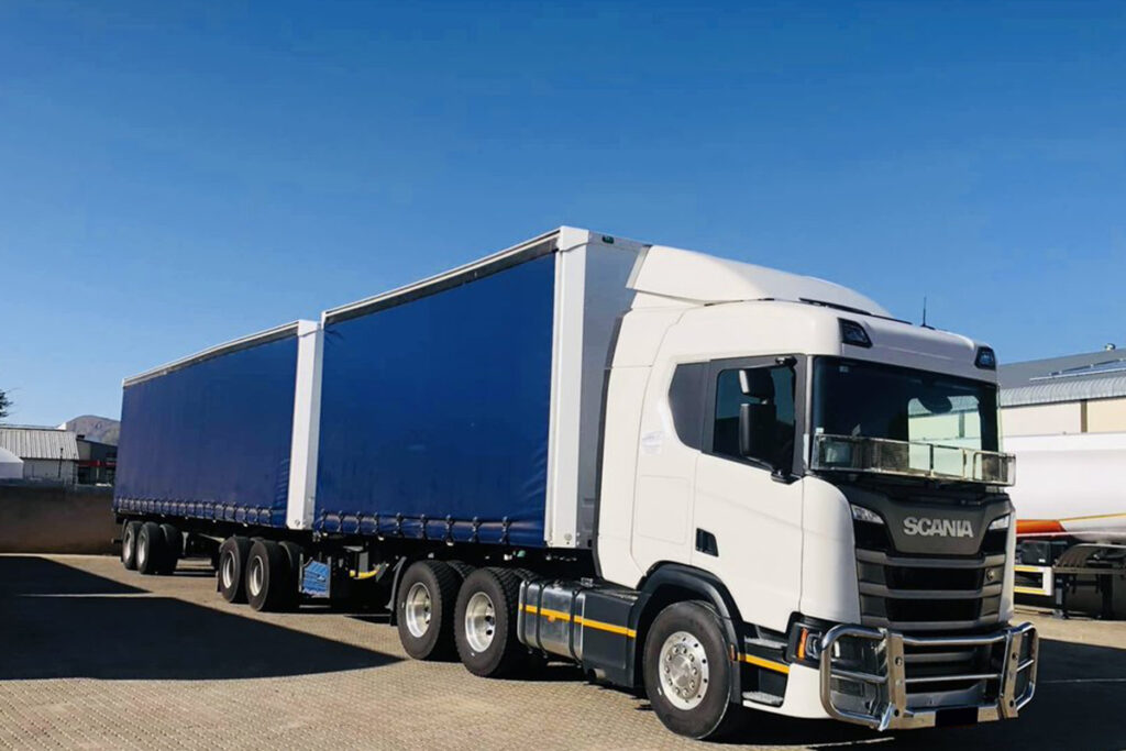 A white truck with a tautliner trailer parked in a paved industrial area