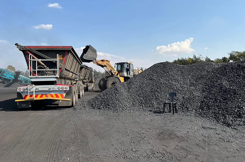 View from behind of a side tipper truck being loaded with coal using a front end loader